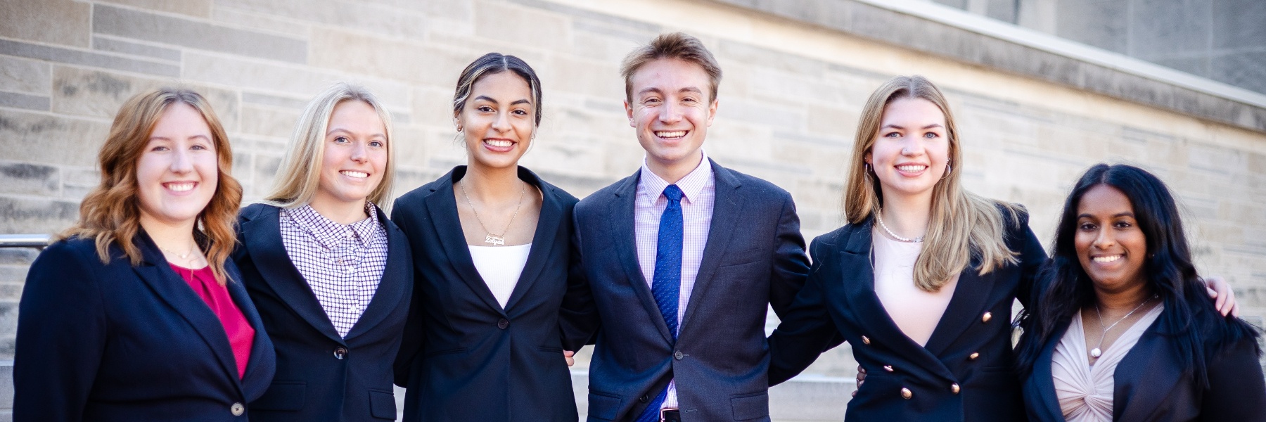 Six smiling students in business attire outside the O'Neill building before a human resource management competition. 